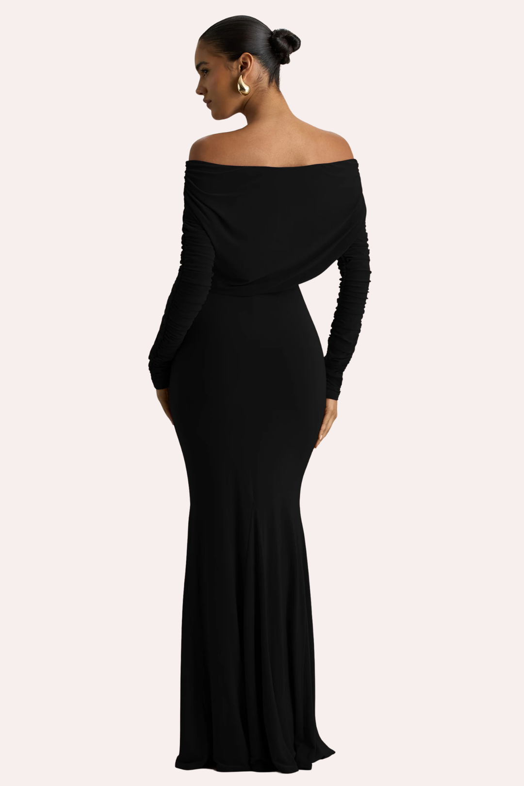 A woman modeling a black off-the-shoulder long-sleeve maxi dress from the back, shown against a solid pale pink background. Available for hire from ourcloset.com.au