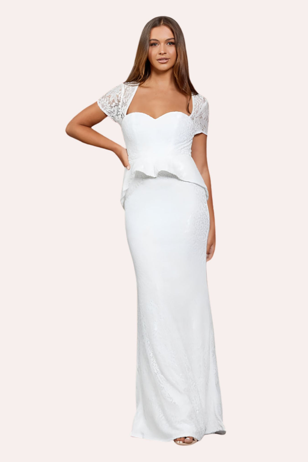 A woman modeling a floor-length white gown with short lace sleeves, a sweetheart neckline, and a peplum waist, photographed against a plain light beige studio background.